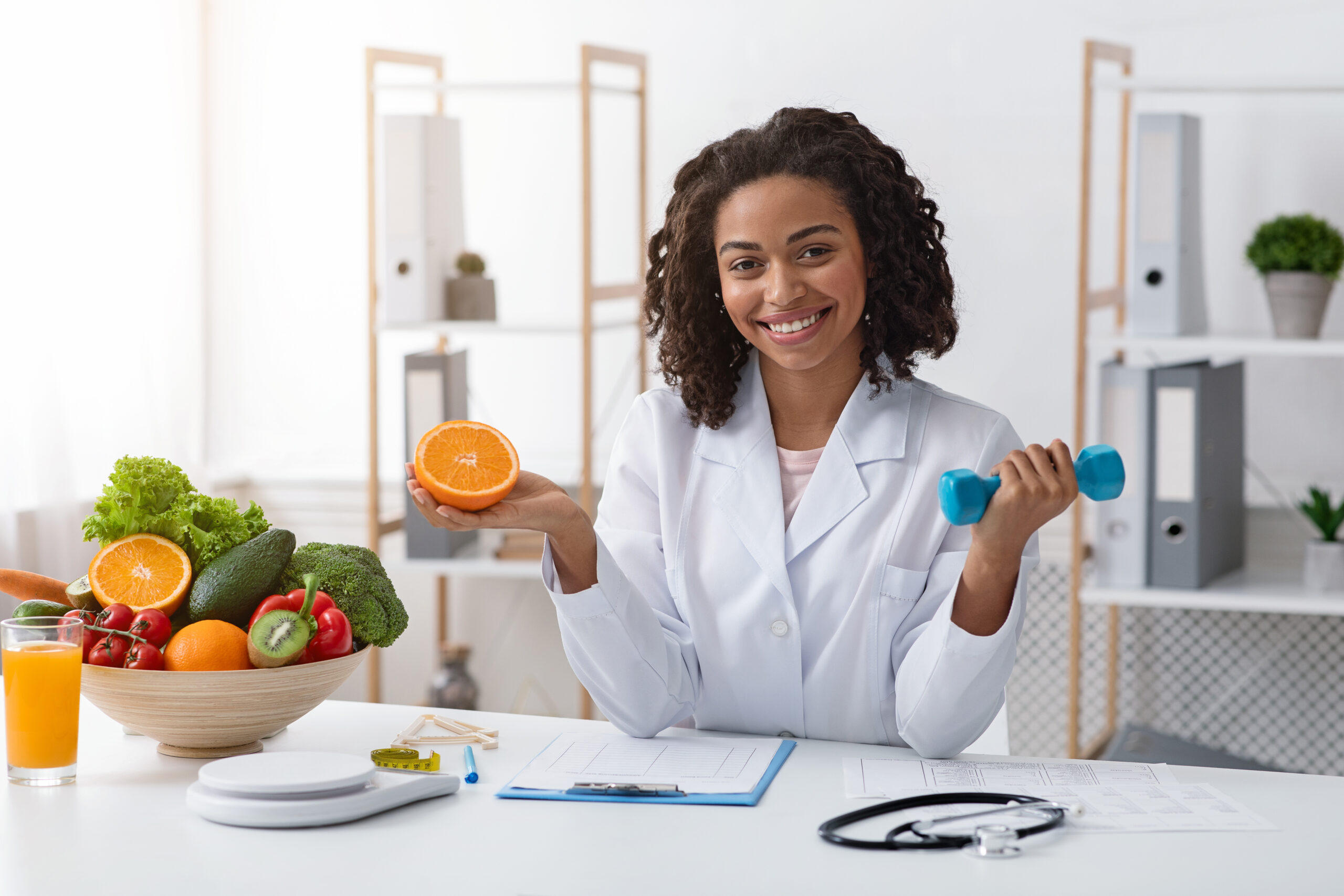 Une nutritionniste tenant une orange et un haltère.
