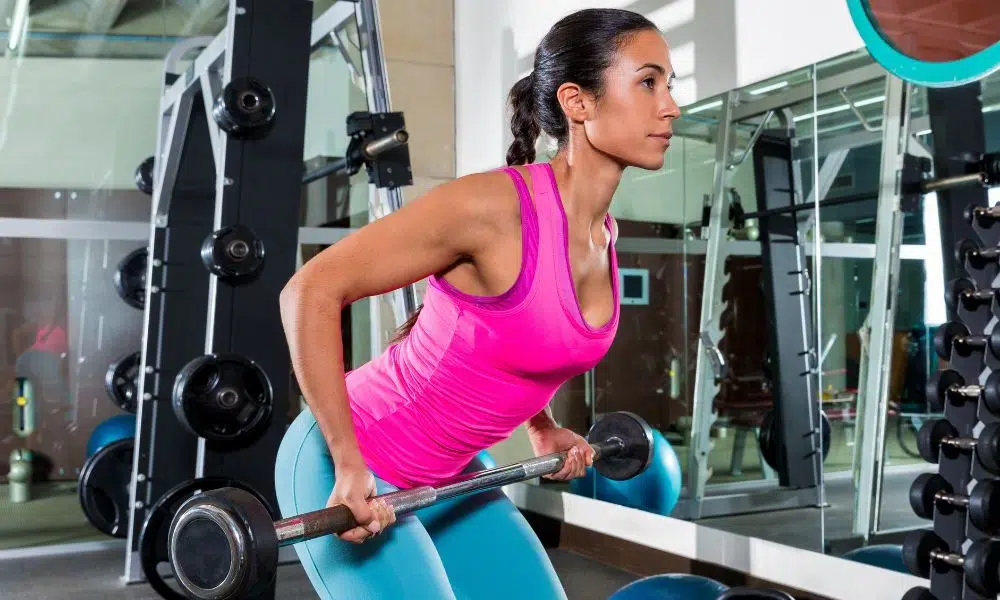 mujer con tirantes rosas haciendo remo con barra