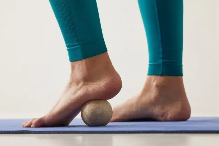 mujer con leggins verdes masajeandose la planta del pie con pelota de masaje