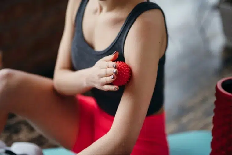 mujer masajeandose el brazo con pelota de masaje roja con picos