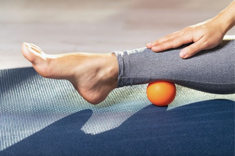 mujer masajeandose el talón con pelota de masaje naranja